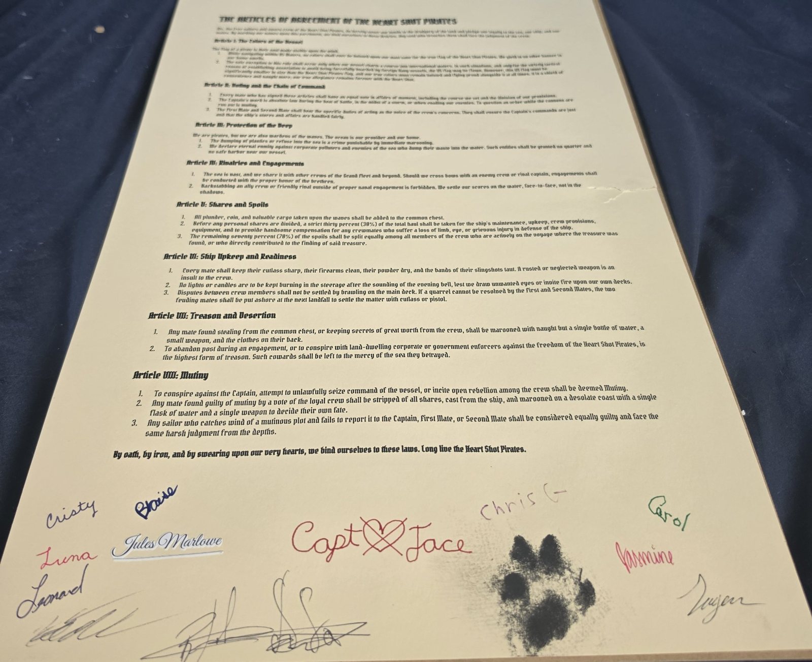 The Articles of Agreement of the Heart Shot Pirates, signed by the crew — Jules Marlowe's signature in navy script among the family's hands, the First Mate's paw print beside the Captain's name.